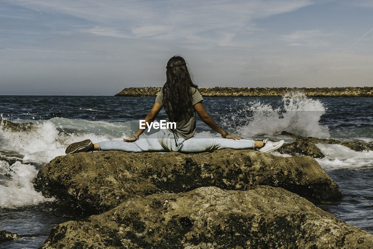 A young women yoga pose on rock at sea shore against sky