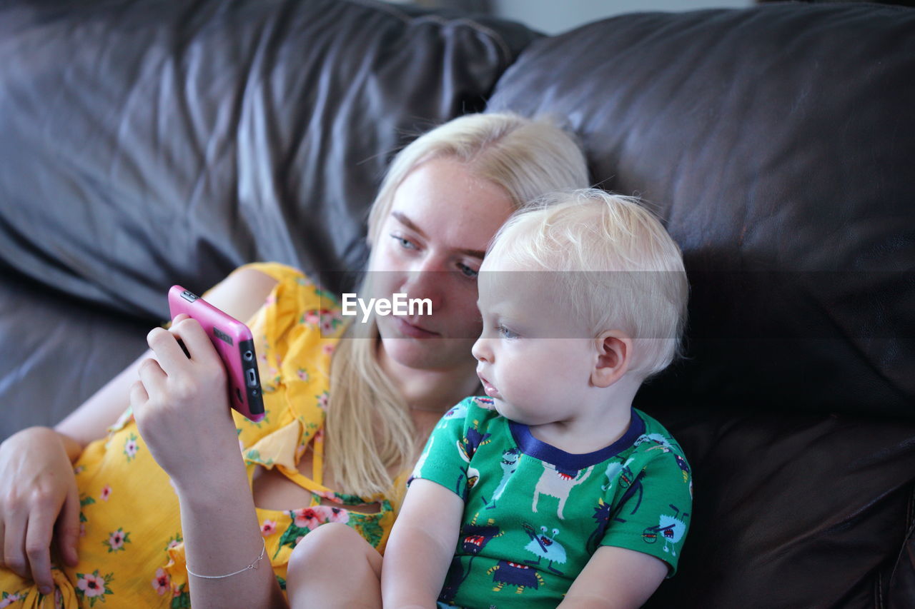High angle view of mother showing phone to baby boy on bed at home