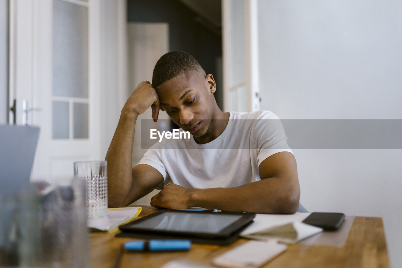 Tired young man leaning on elbow while studying at home