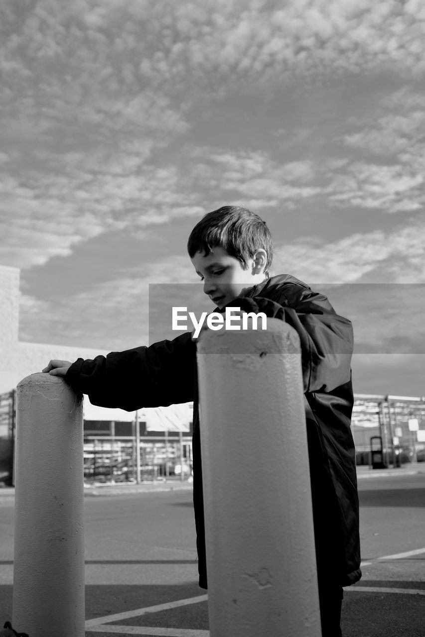 Boy standing by bollards on street against sky