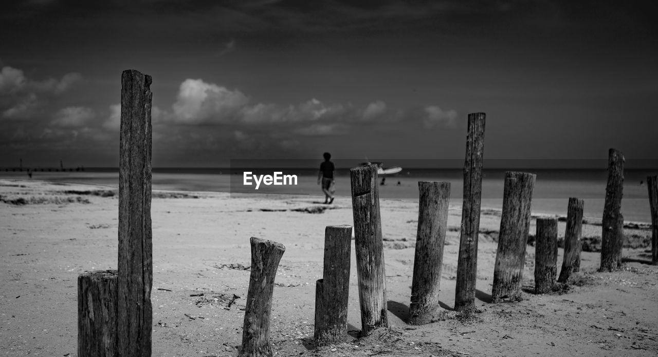 MAN STANDING ON WOODEN POST ON BEACH