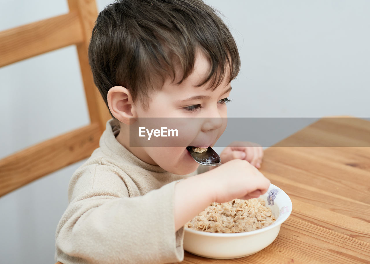 Little boy eating oatmeal for breakfast in the kitchen