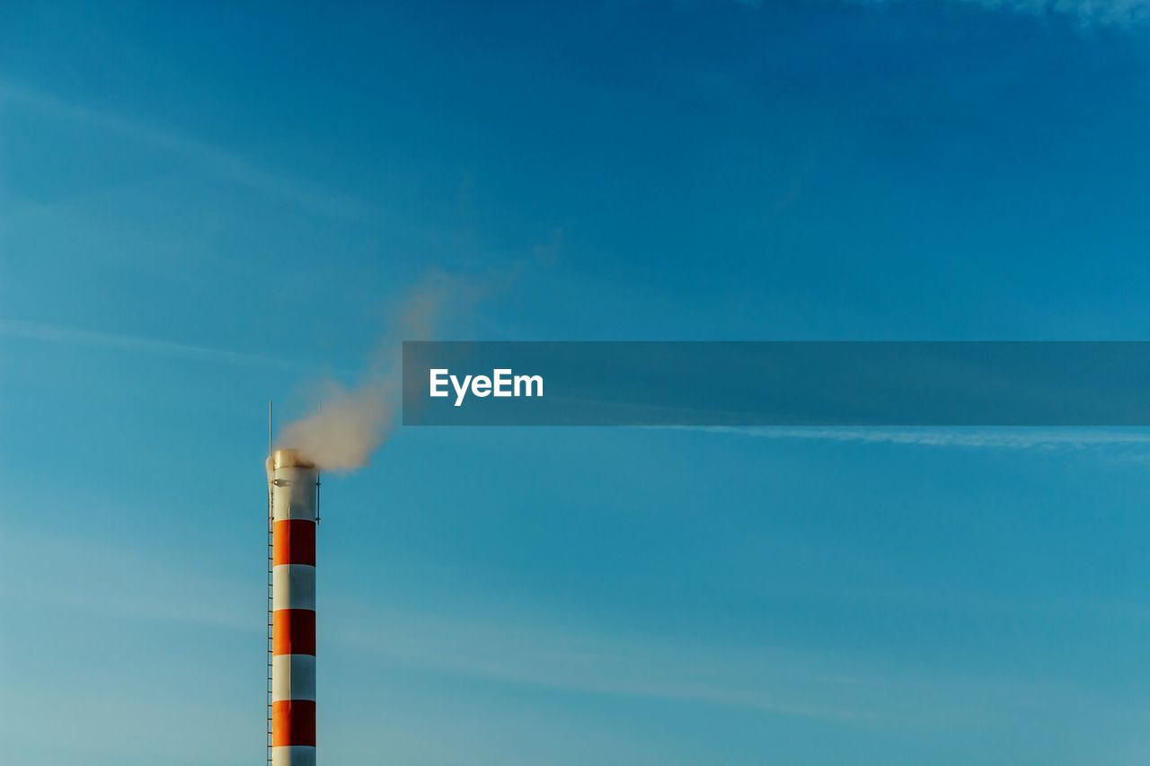 Low angle view of smoke emitting from chimney against blue sky