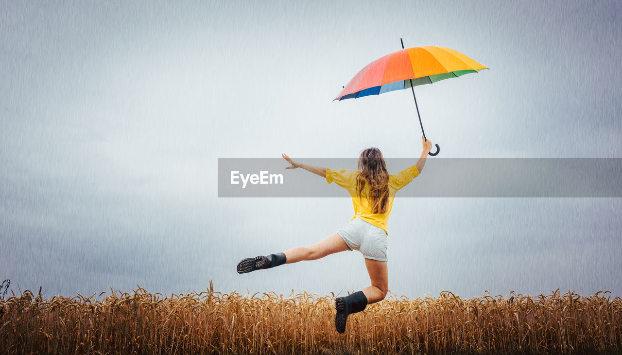 Rear view of woman holding umbrella while levitating against cloudy sky