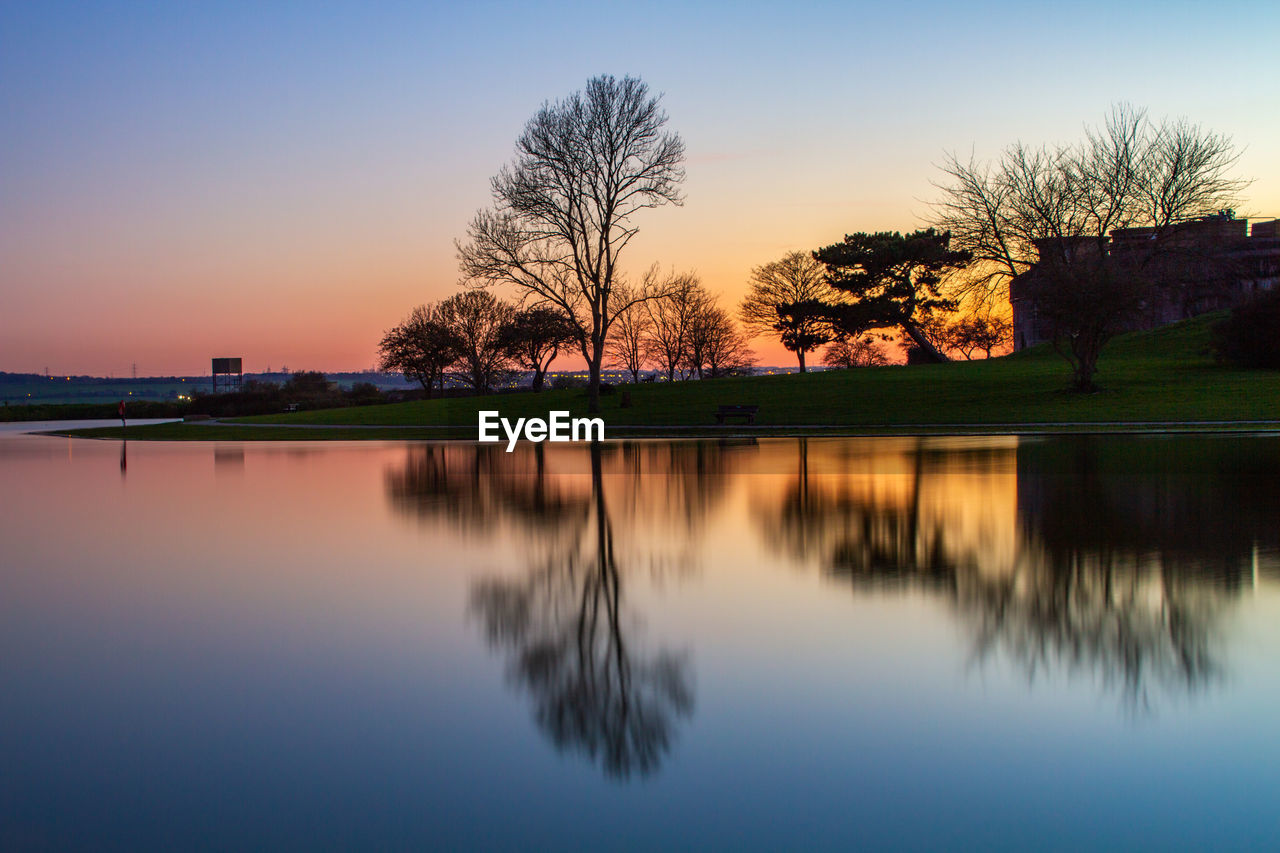 reflection, water, sky, tree, morning, dawn, nature, lake, tranquility, beauty in nature, plant, scenics - nature, tranquil scene, sunrise, no people, landscape, environment, blue, outdoors, travel destinations, twilight, idyllic, orange color, horizon, architecture