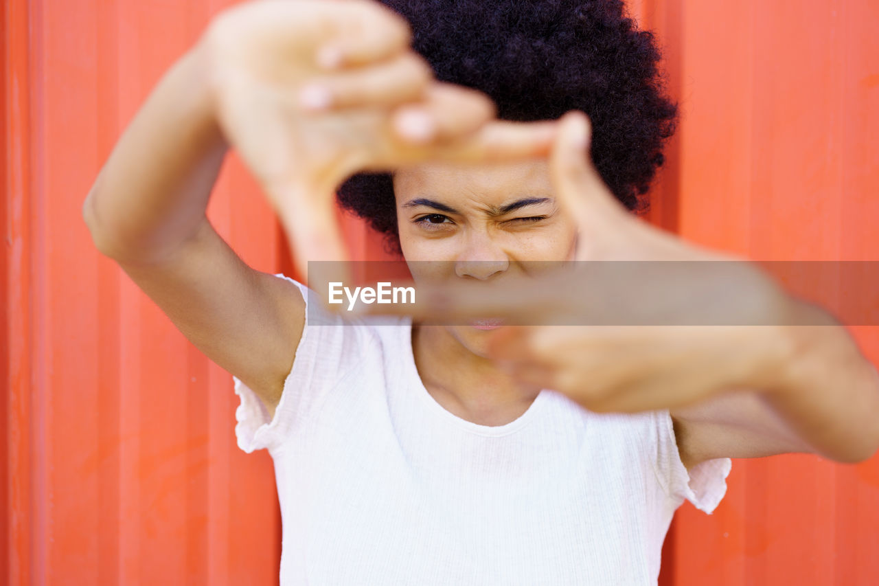 Portrait of woman making finger frame in front of red wall