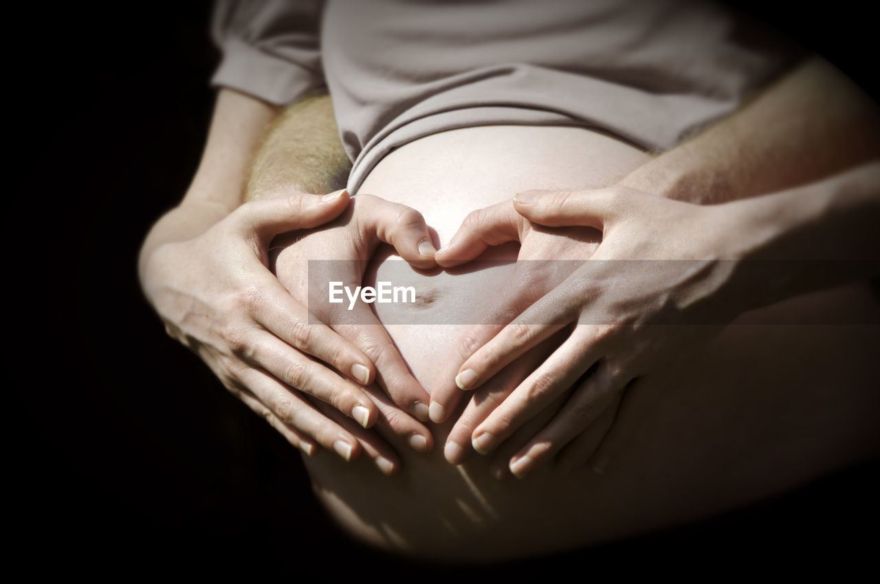 Midsection of pregnant woman holding stomach against black background