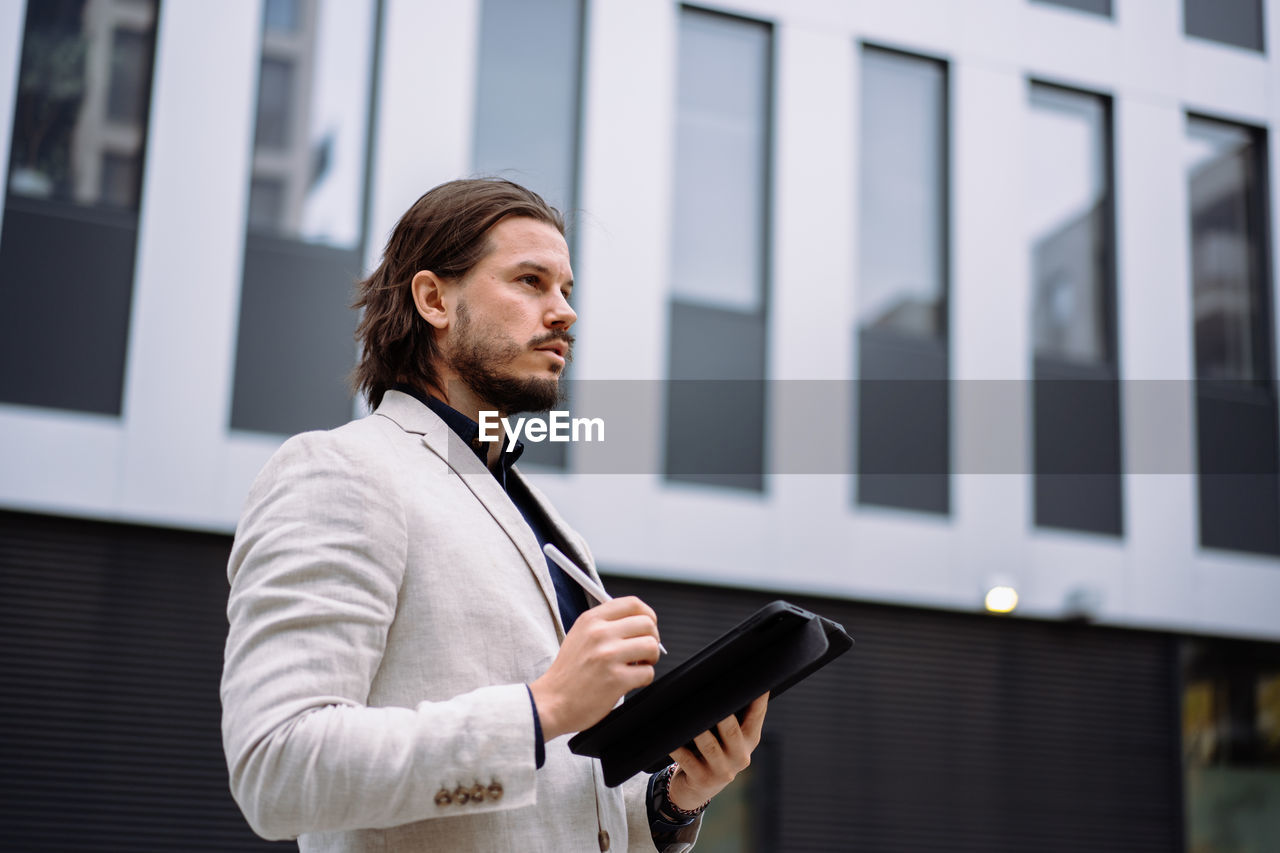 Smart businessman writing on tablet device outdoors near the business center