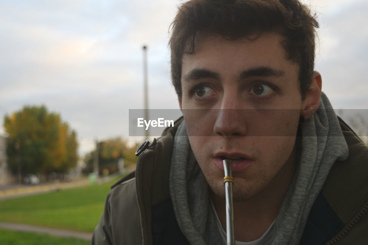 Close-up of young man with metal against sky