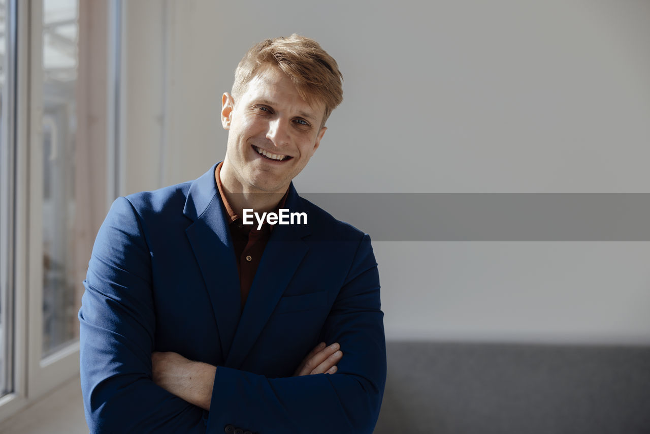 Smiling businessman with arms crossed standing in office