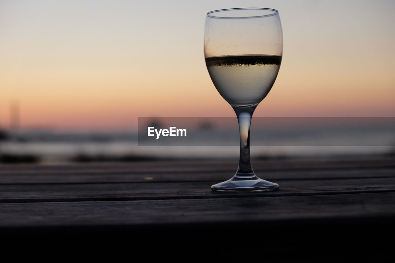 Close-up of drink on wooden table against sky during sunset