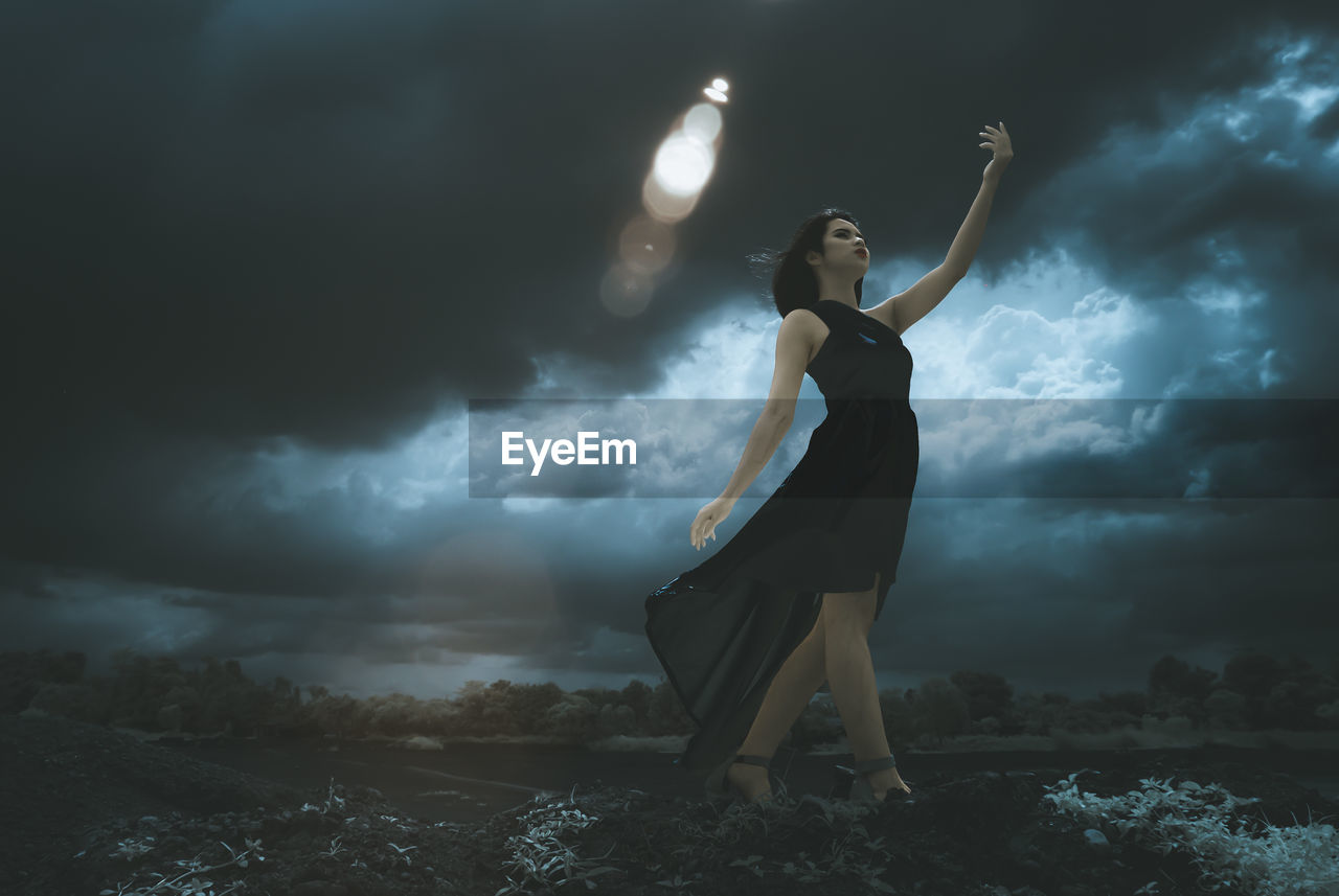 Young woman standing against cloudy sky