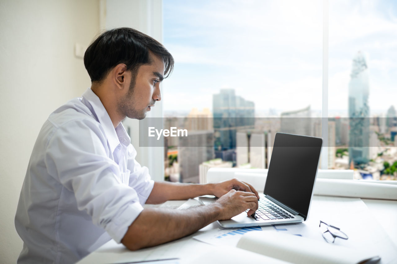 Side view of businessman using laptop at desk in office