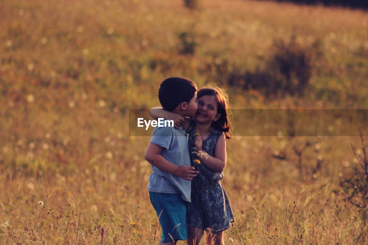 Boy kissing friend while standing on field