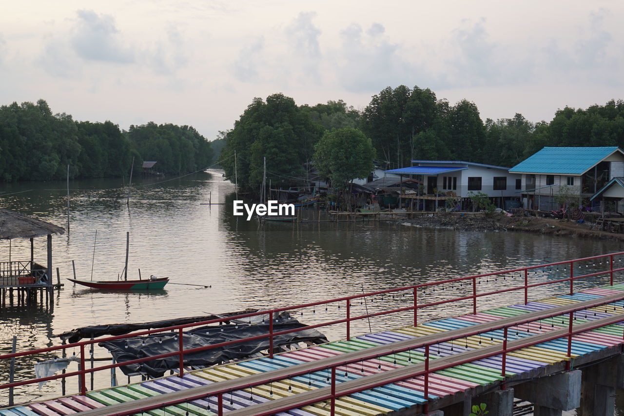 Scenic view of river by trees and houses against sky