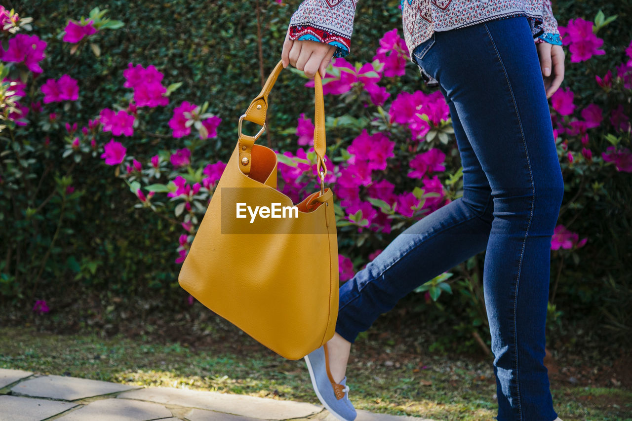 Low section of woman holding purse while walking on footpath