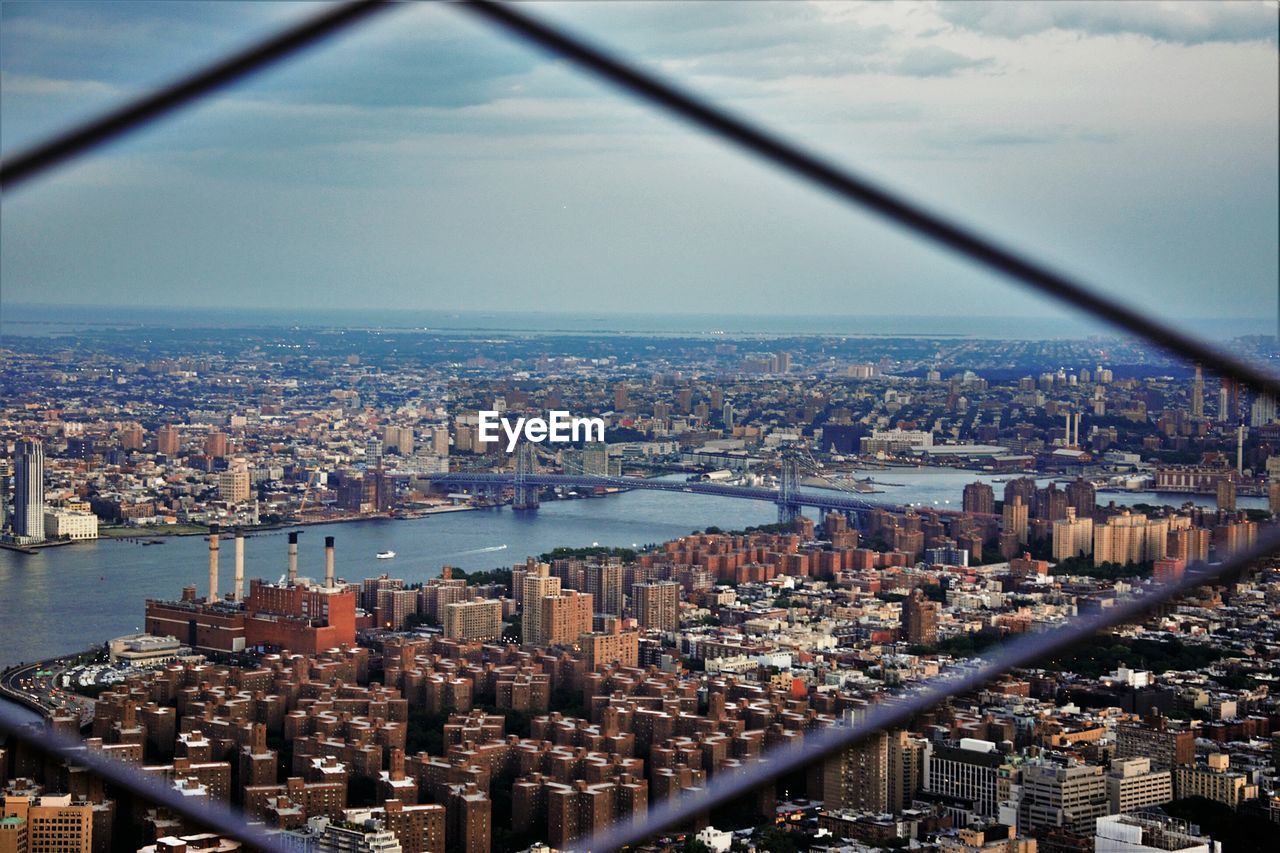 East river amidst cityscape against sky seen through fence