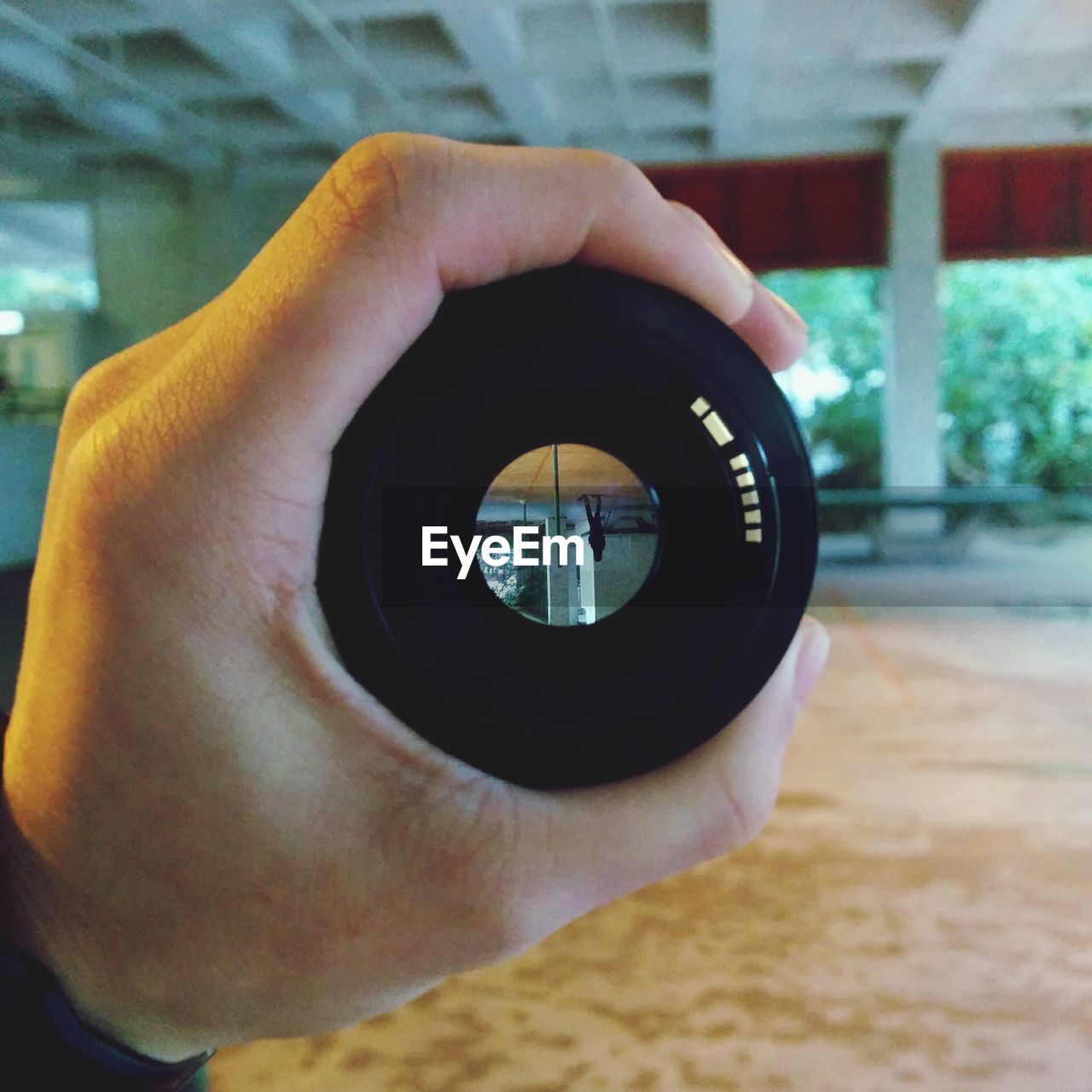 Cropped hand holding camera lens with woman reflection in it