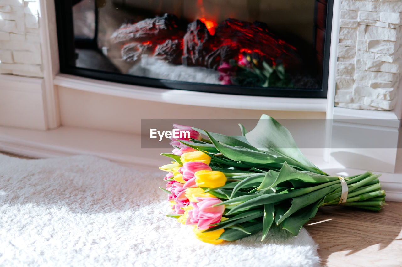 Fresh spring yellow and pink tulips bouquet on the fur carpet by the fireplace with copy space