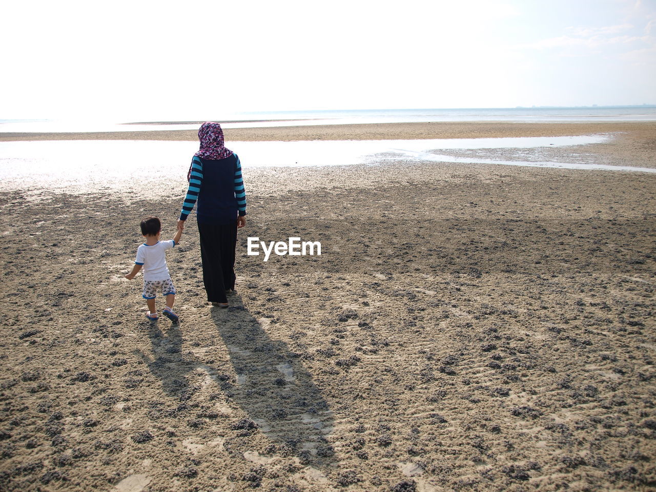 Rear view of mother with her son walking at beach