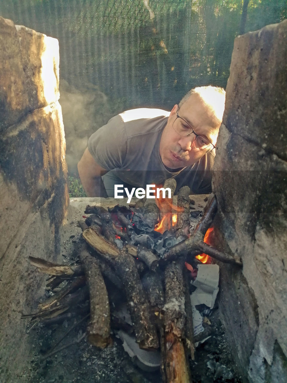Low angle view of man relaxing on wooden log, preparing bbq 