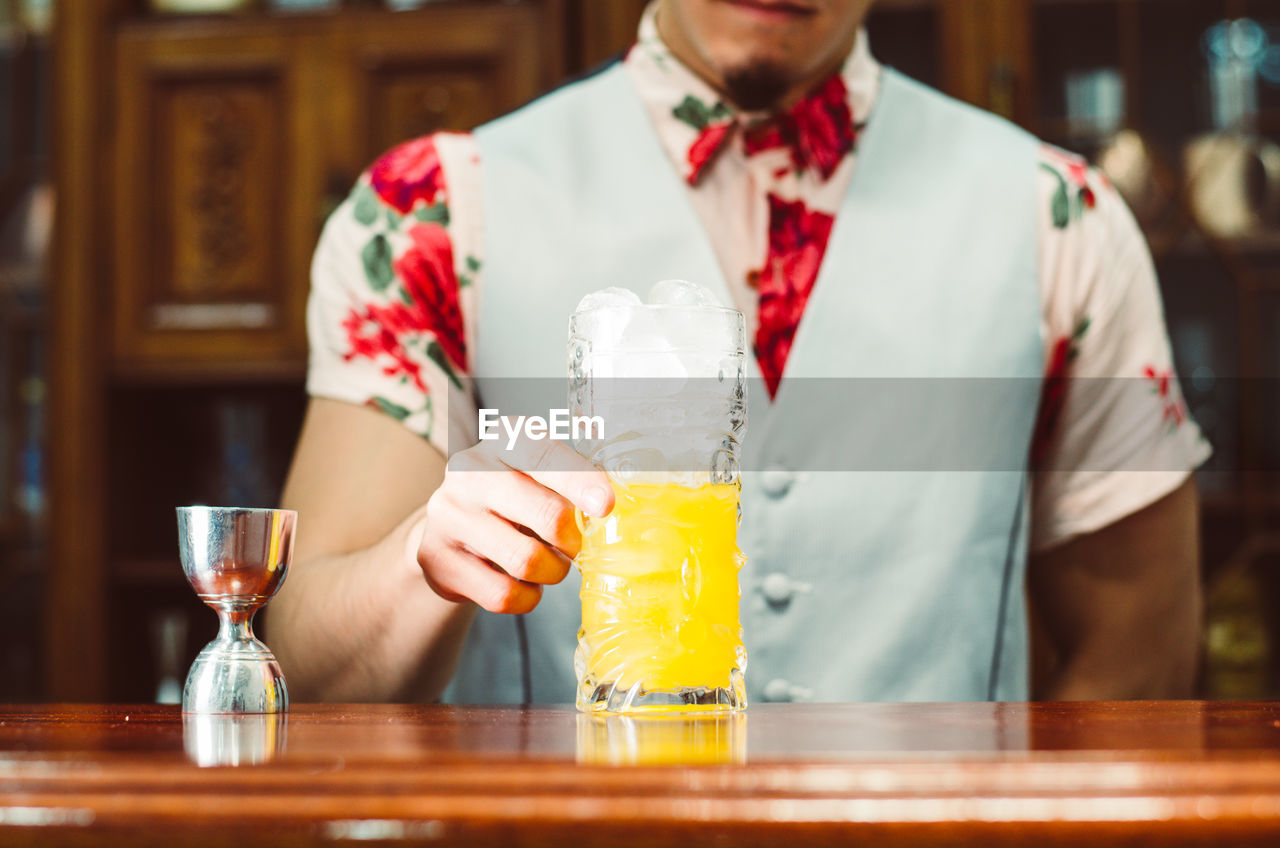 Midsection of bartender holding drink at bark