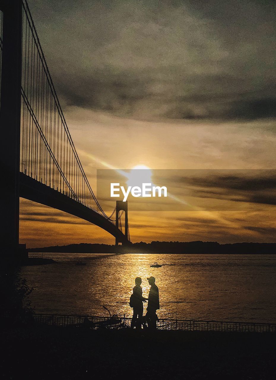 Silhouette of suspension bridge over river during sunset