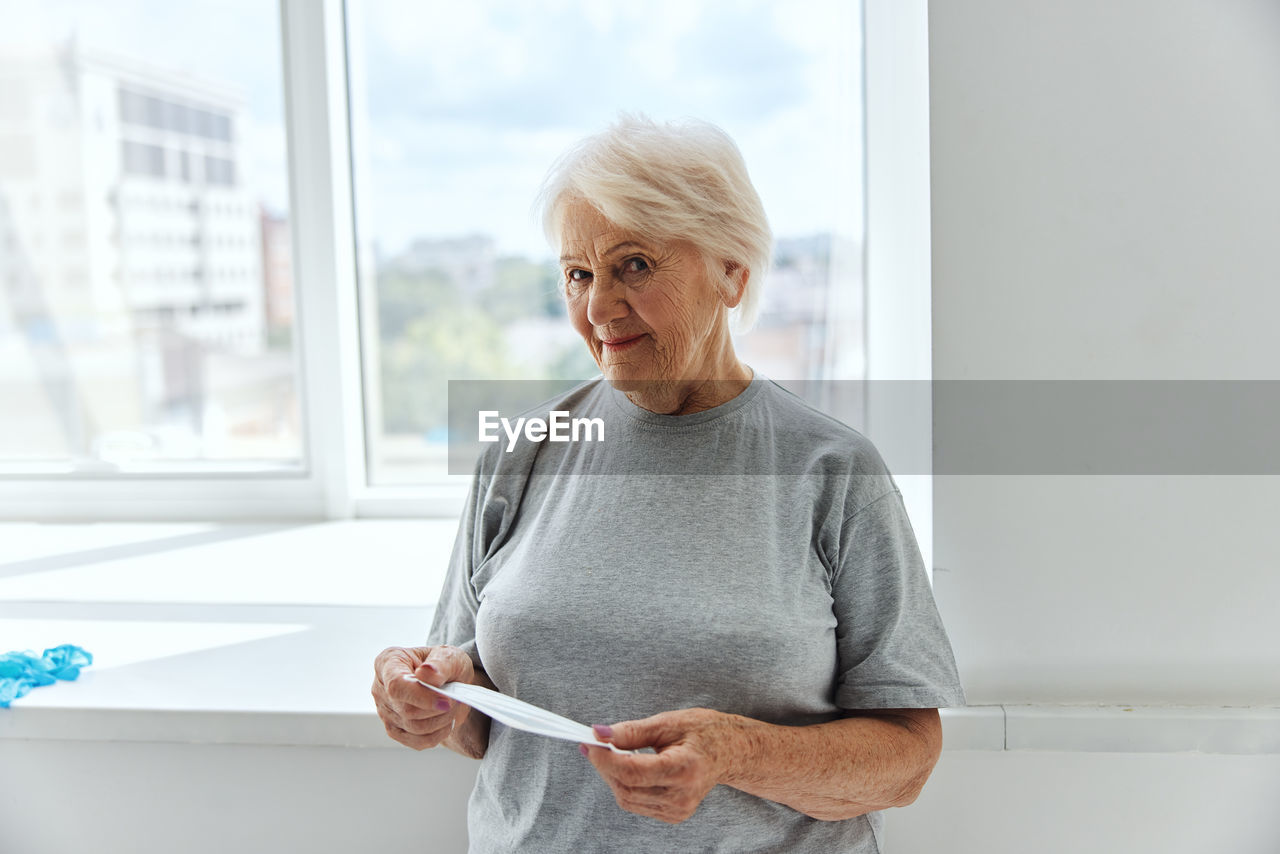 MID ADULT WOMAN STANDING BY WINDOW