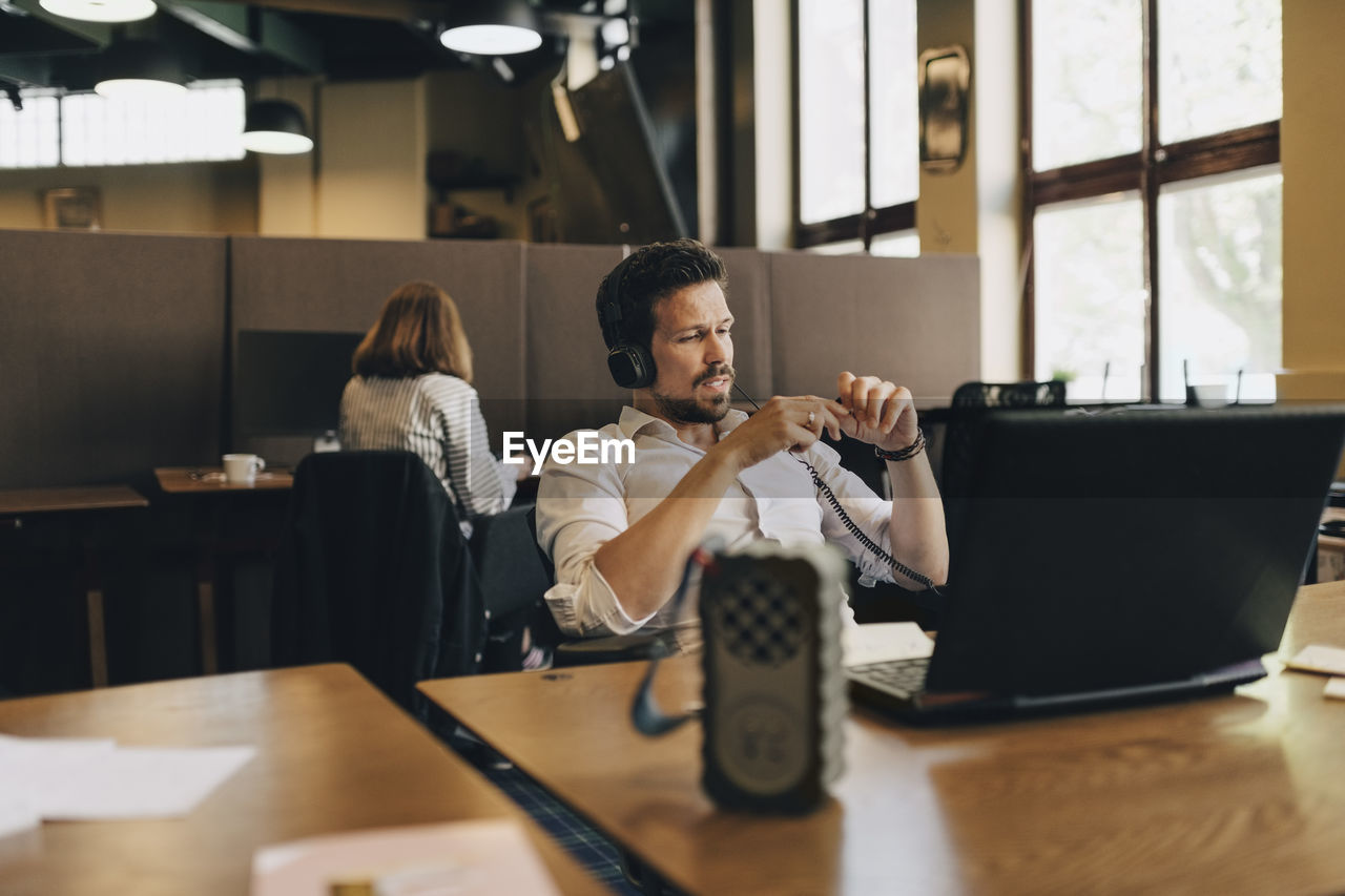 Creative businessman wearing headphones while video conferencing on laptop in office