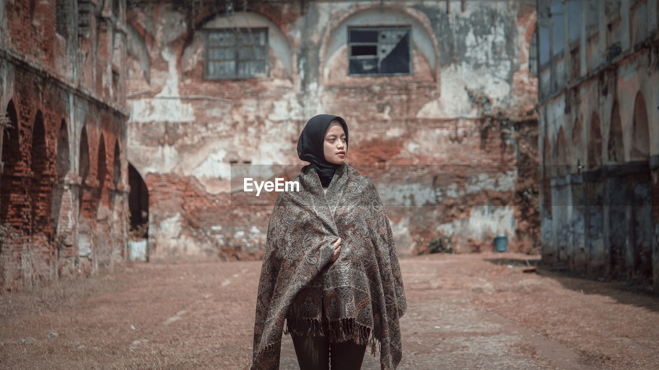 PORTRAIT OF WOMAN STANDING AGAINST BUILDINGS IN CITY