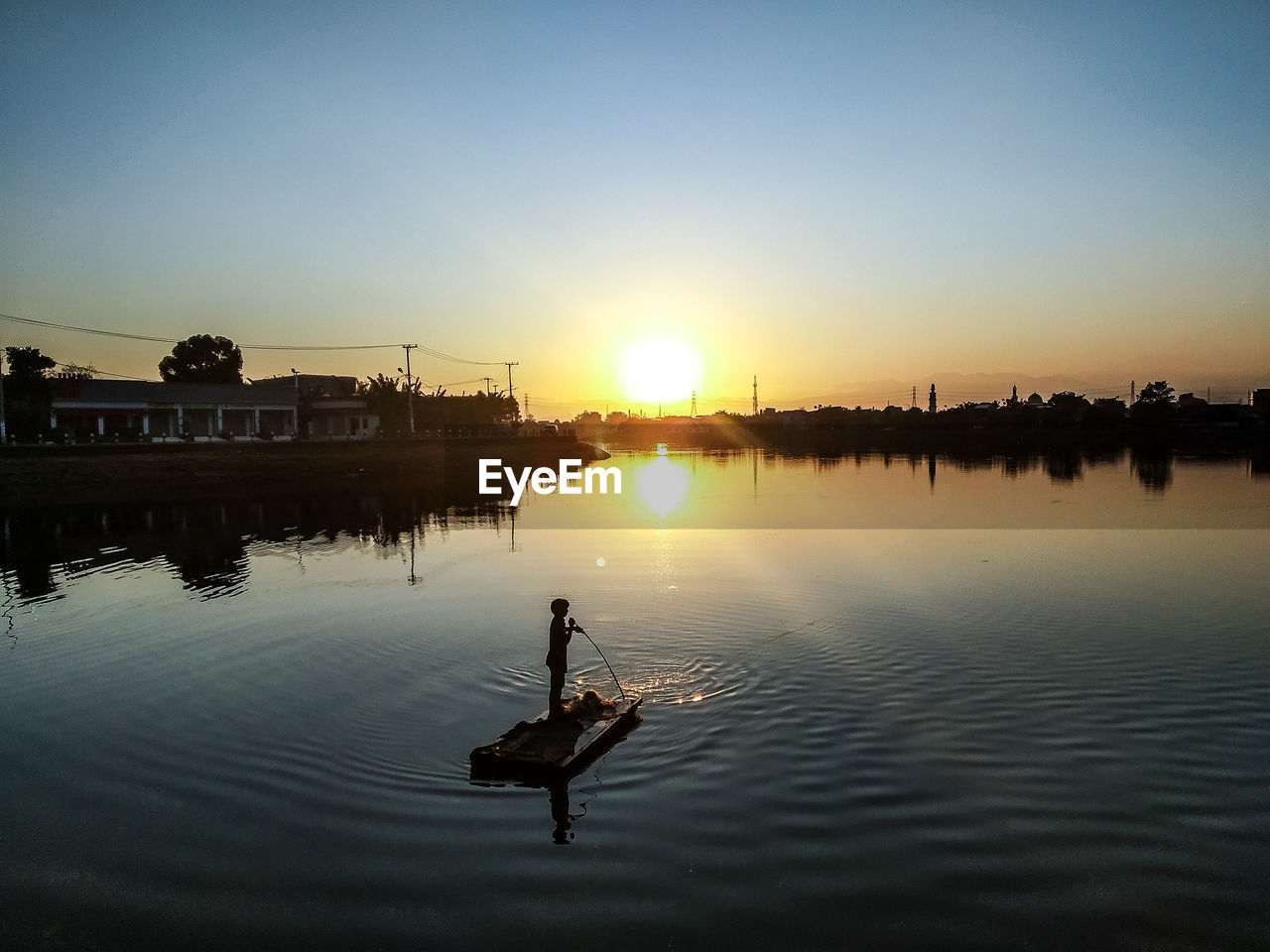 Silhouette man in wooden raft in lake against sky during sunset