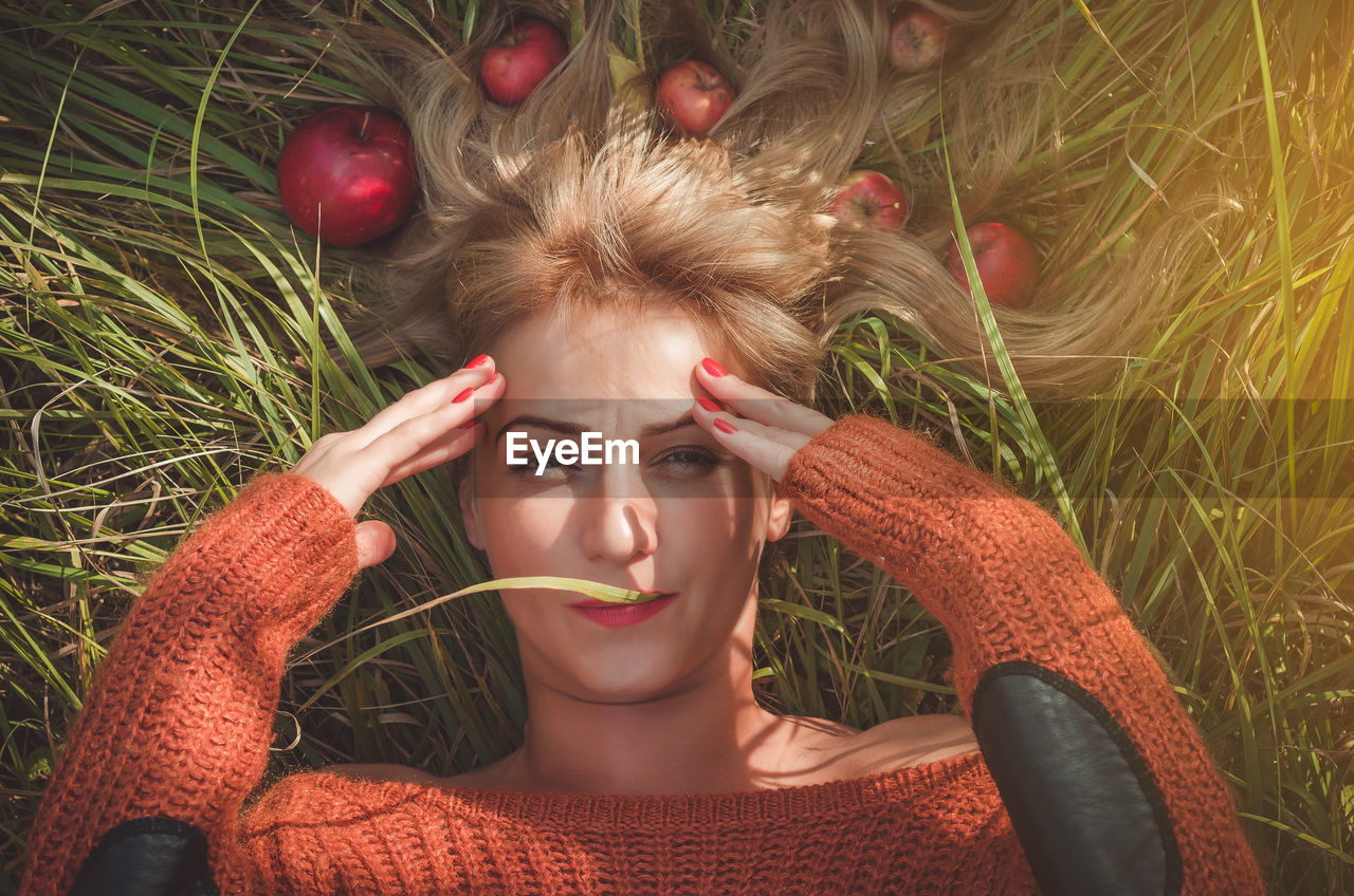 Directly above portrait of woman lying with apples on grassy field