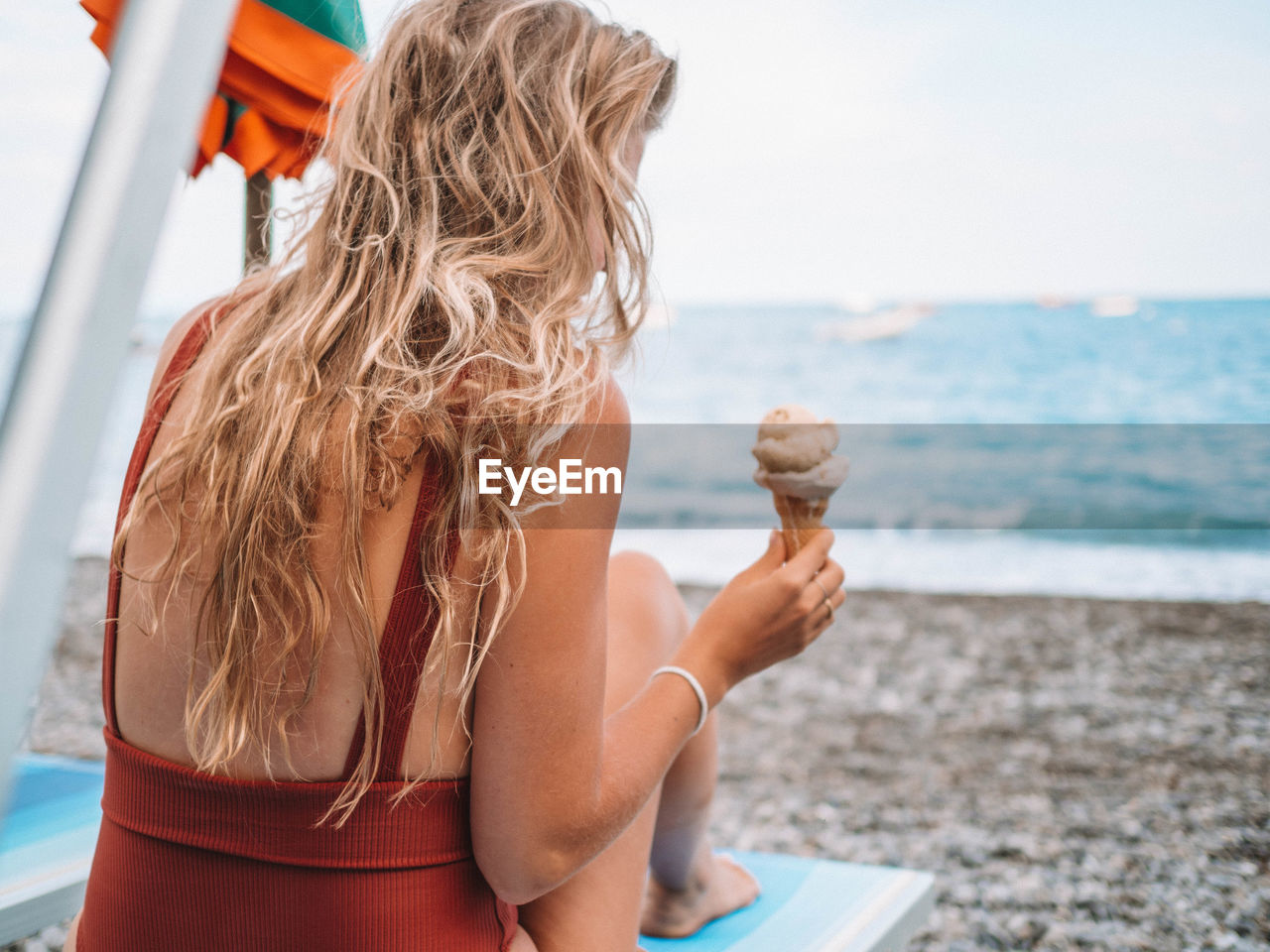 Woman with ice cream sitting on lounge chair at beach