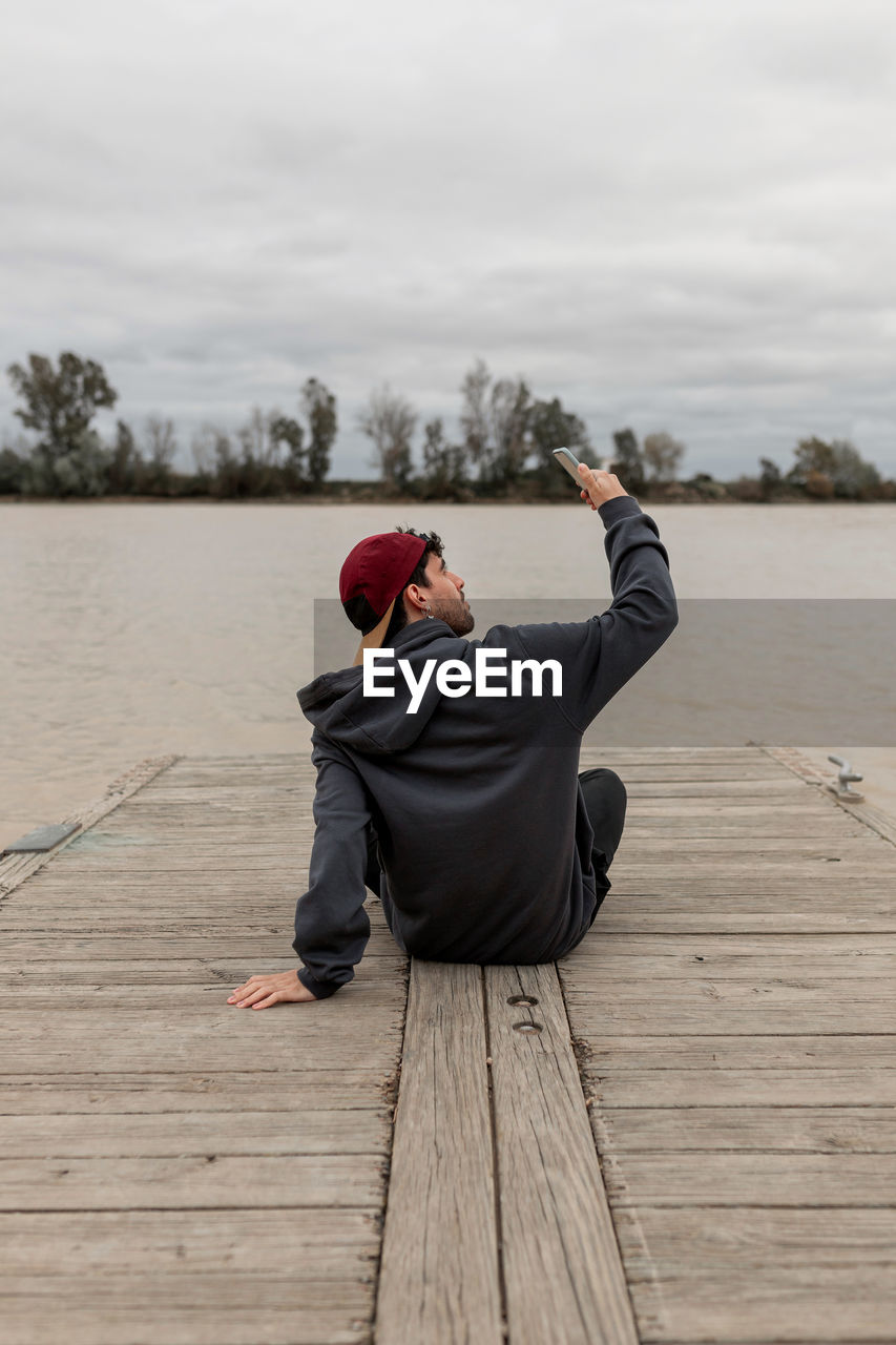 Side view of man using mobile phone while sitting on wood