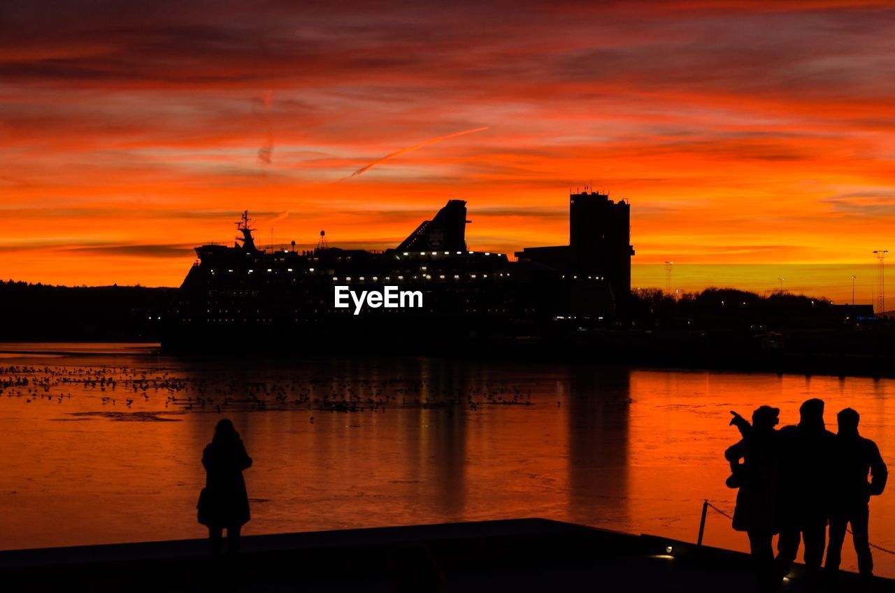 SILHOUETTE PEOPLE ON ILLUMINATED CITY AGAINST ORANGE SKY