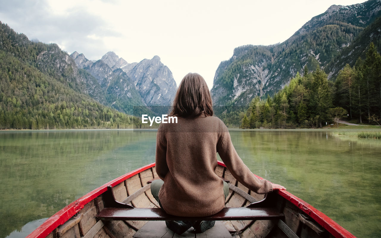 Rear view of woman boating on lake against mountains