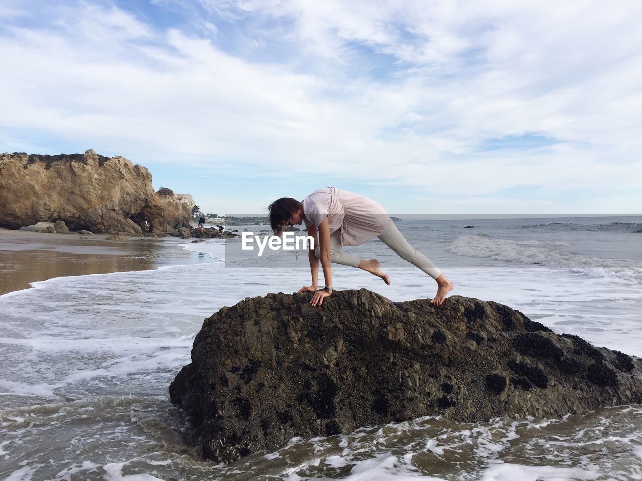 Woman practicing yoga at beach against sky