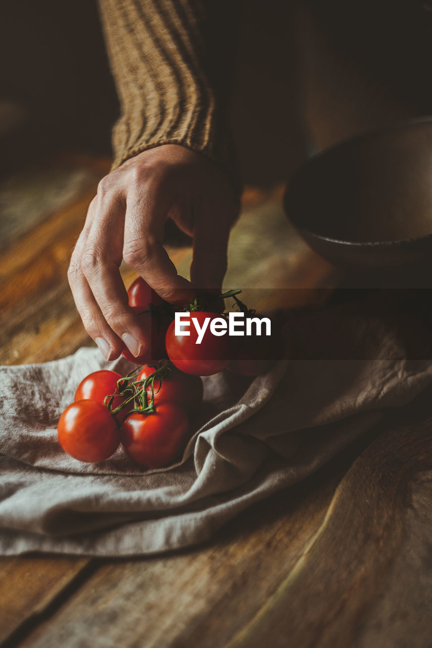 Cropped hand of woman holding cherry tomatoes on table