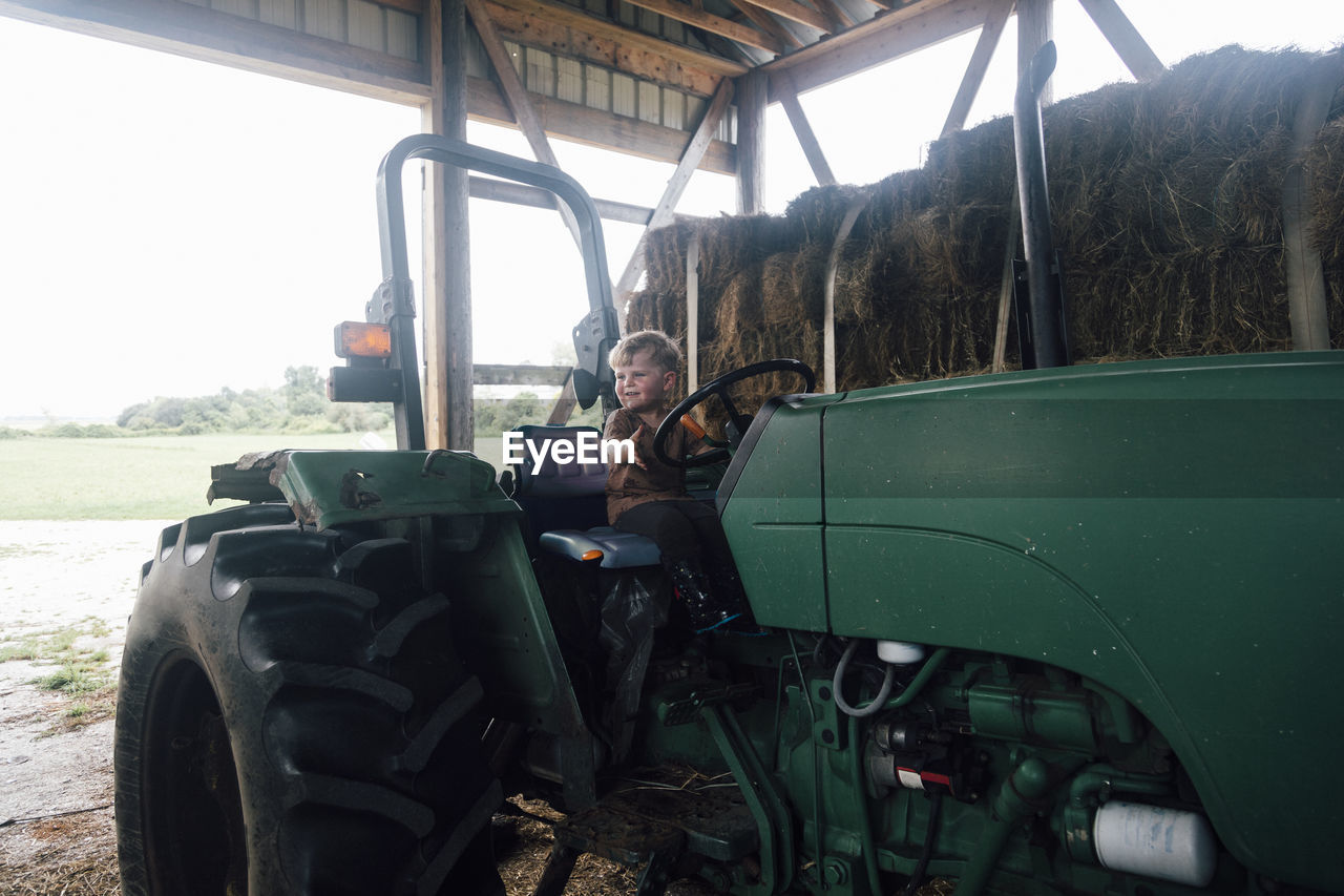 Happy boy sitting on tractor's driving seat in farm