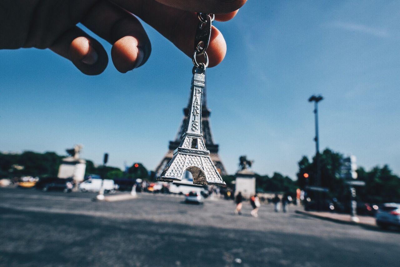 Cropped image of hand holding key ring against eiffel tower