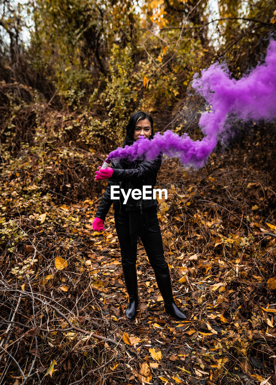 Young woman holding distress flare while standing in forest during autumn