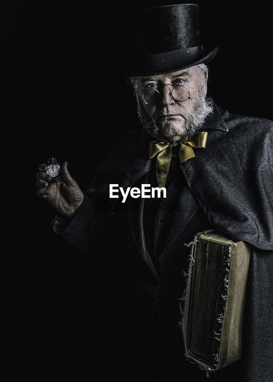 Portrait of beardy man wearing hat against black background, looking like scrooge