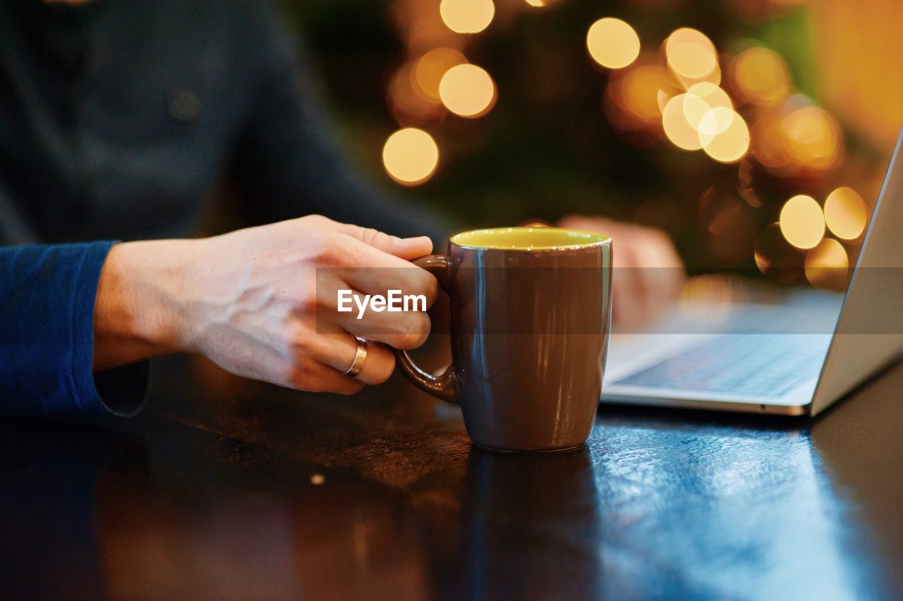 Midsection of man holding coffee cup on table at cafe