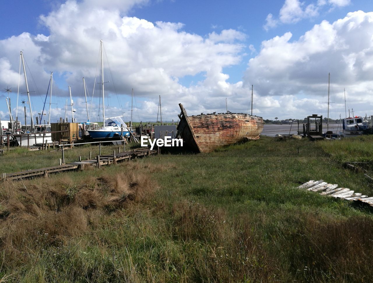 SAILBOATS MOORED ON FIELD BY GRASS AGAINST SKY