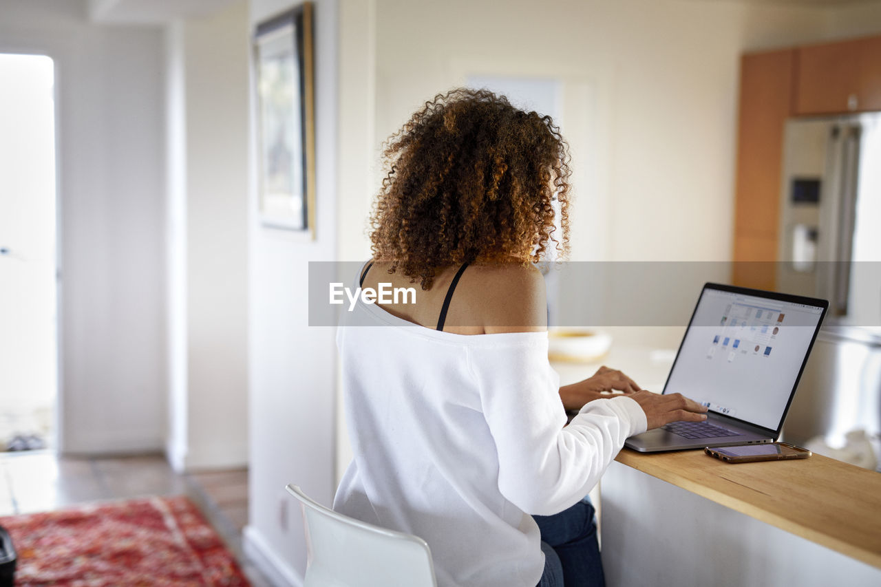 Rear view of woman using laptop computer while sitting at home