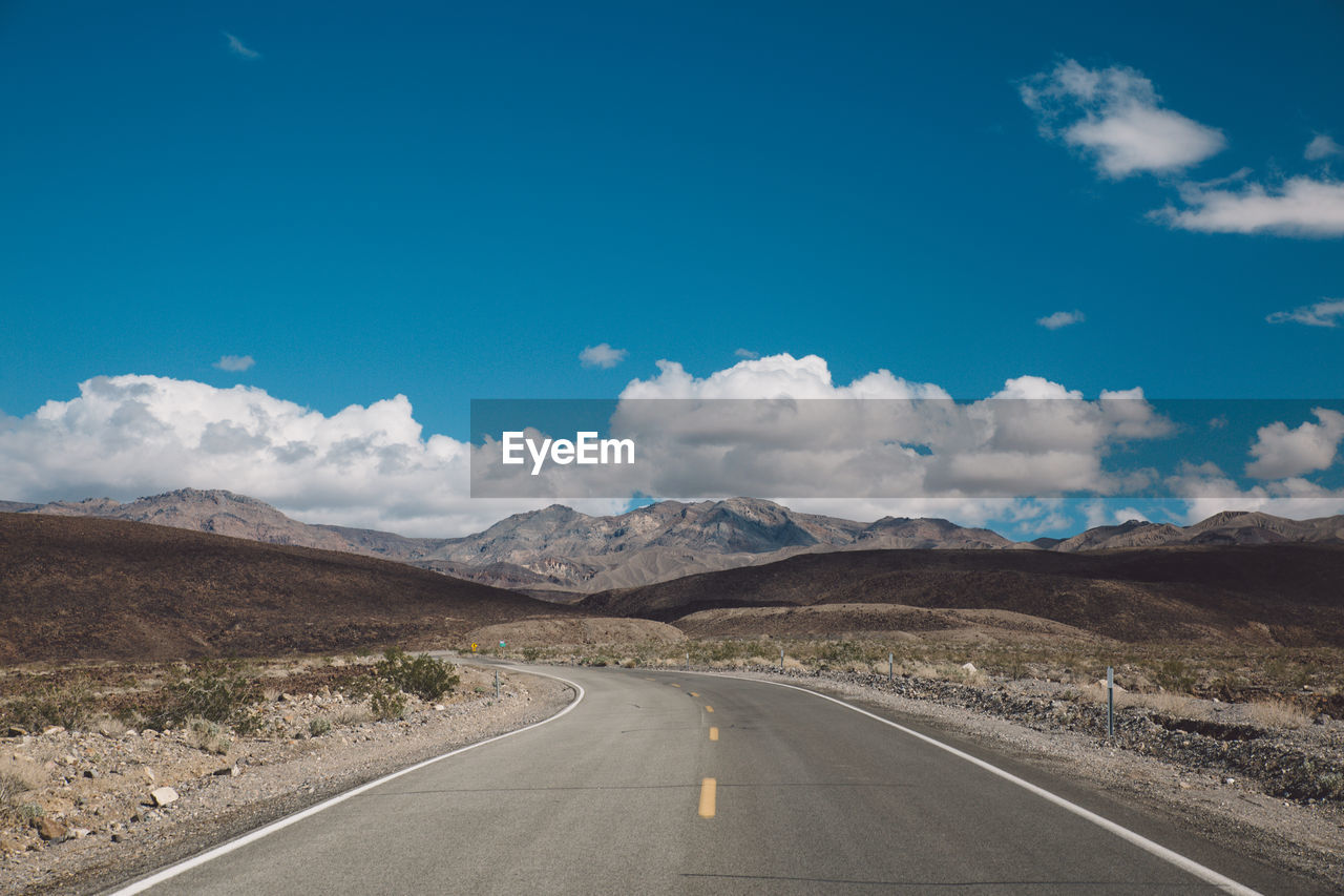 Empty road by mountains against blue sky