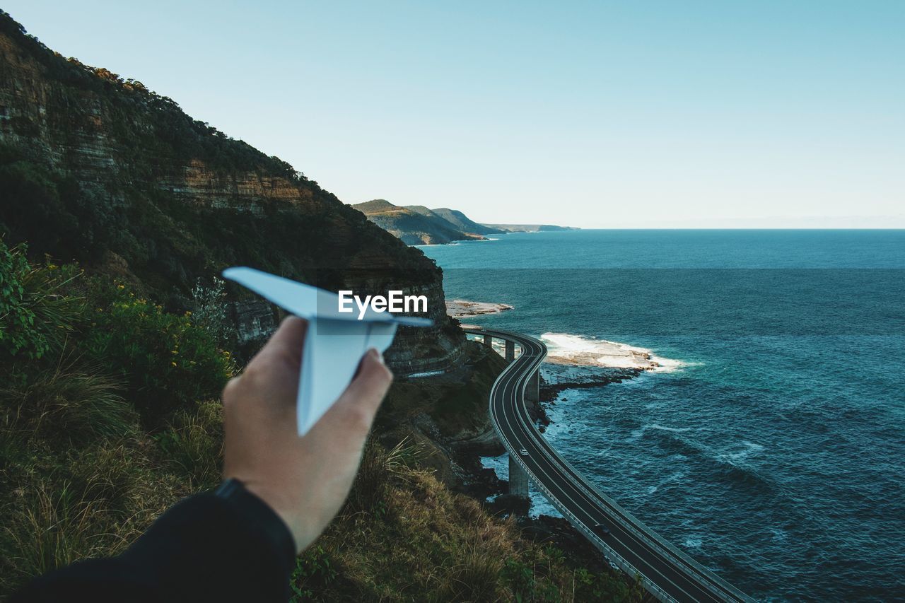 Cropped image of hand holding paper airplane against sea