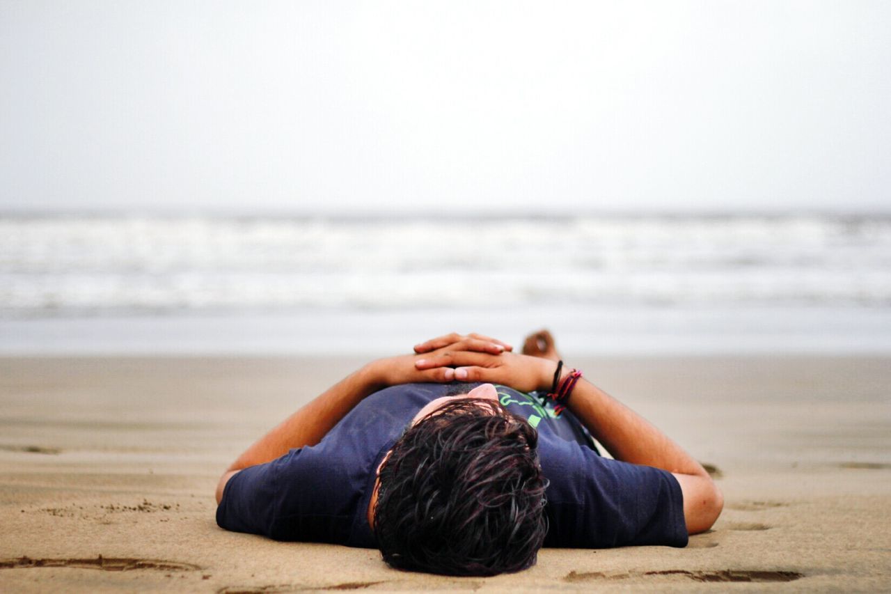 Rear view of man relaxing at beach against sky