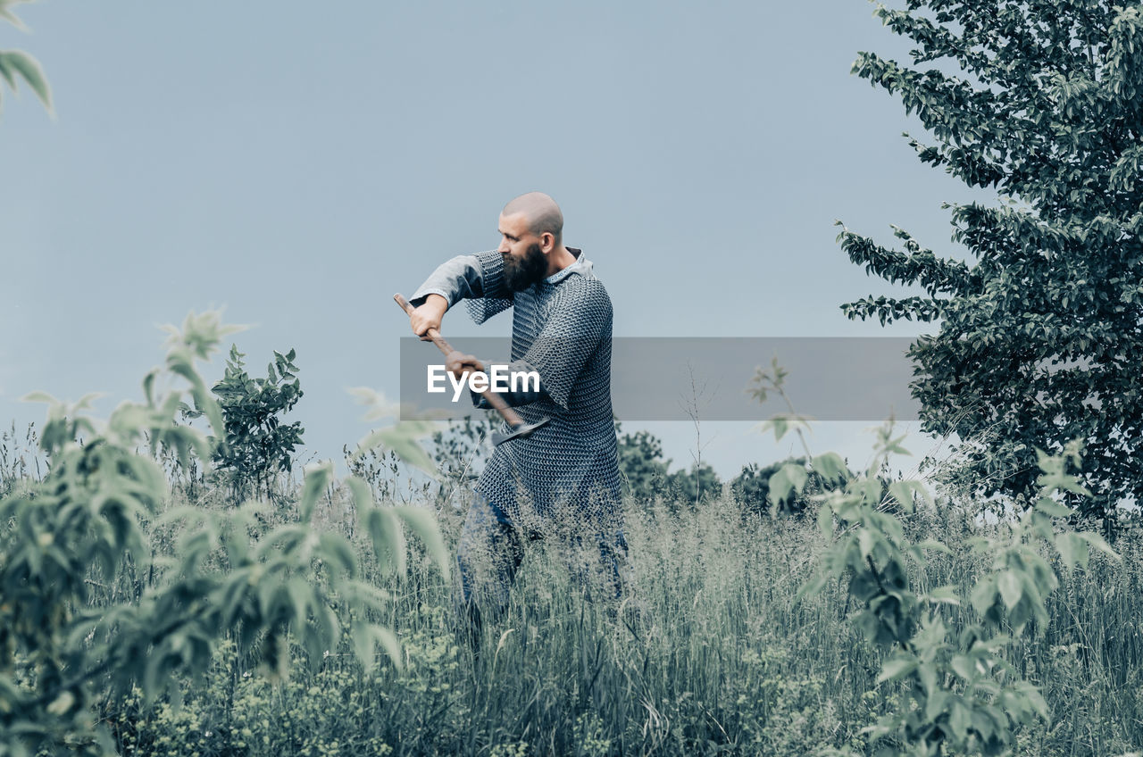 Emotional photo of medieval viking in metal chain mail swinging ax. background of green grass