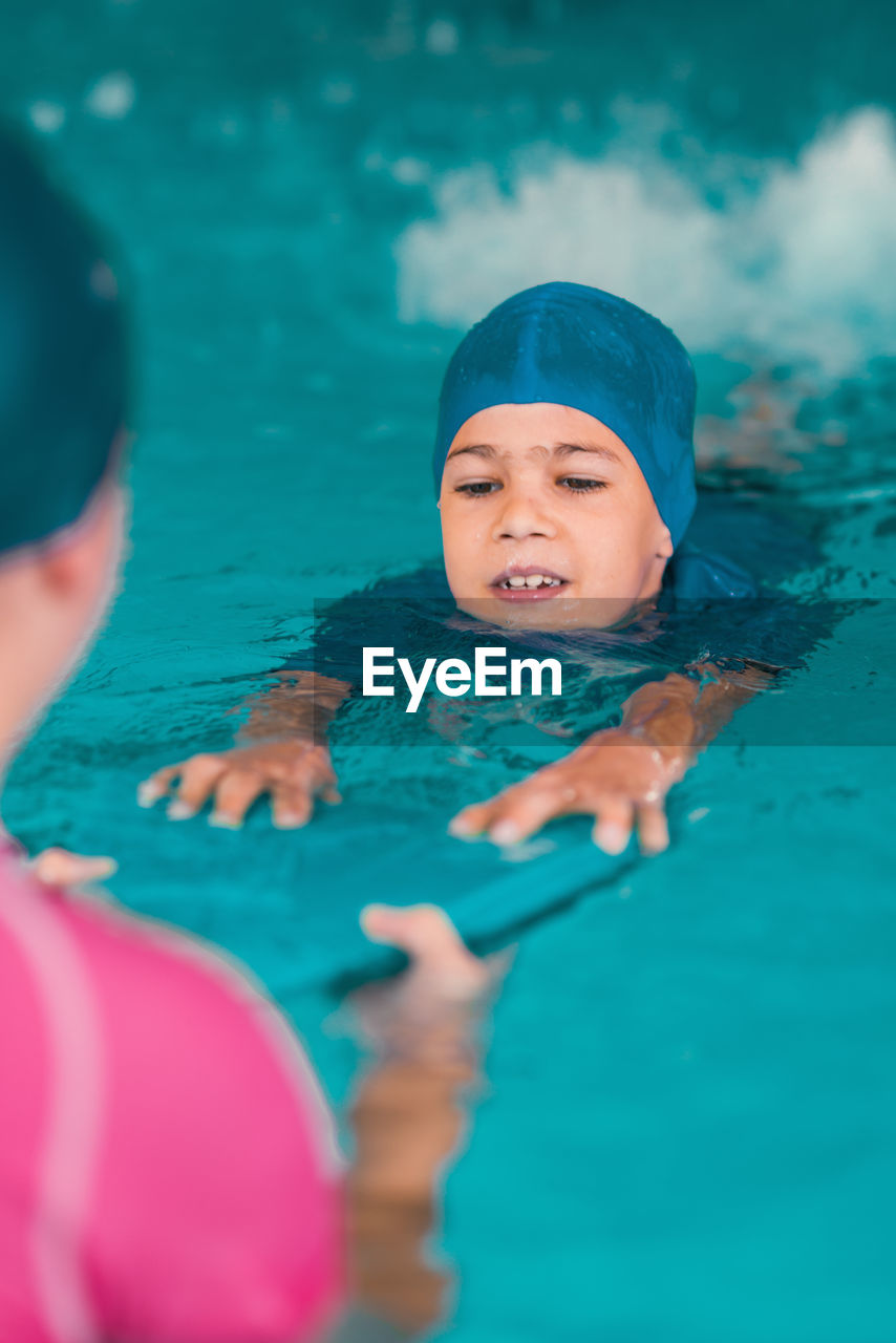 Boy learning to swim in pool with teacher